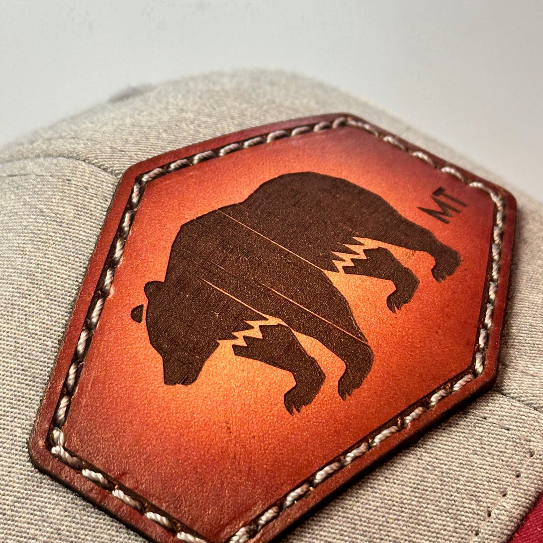 A close up of a made in Montana hand dyed leather patch of an etched Bear silhouette and MT, sewn on a Richardson trucker hat.