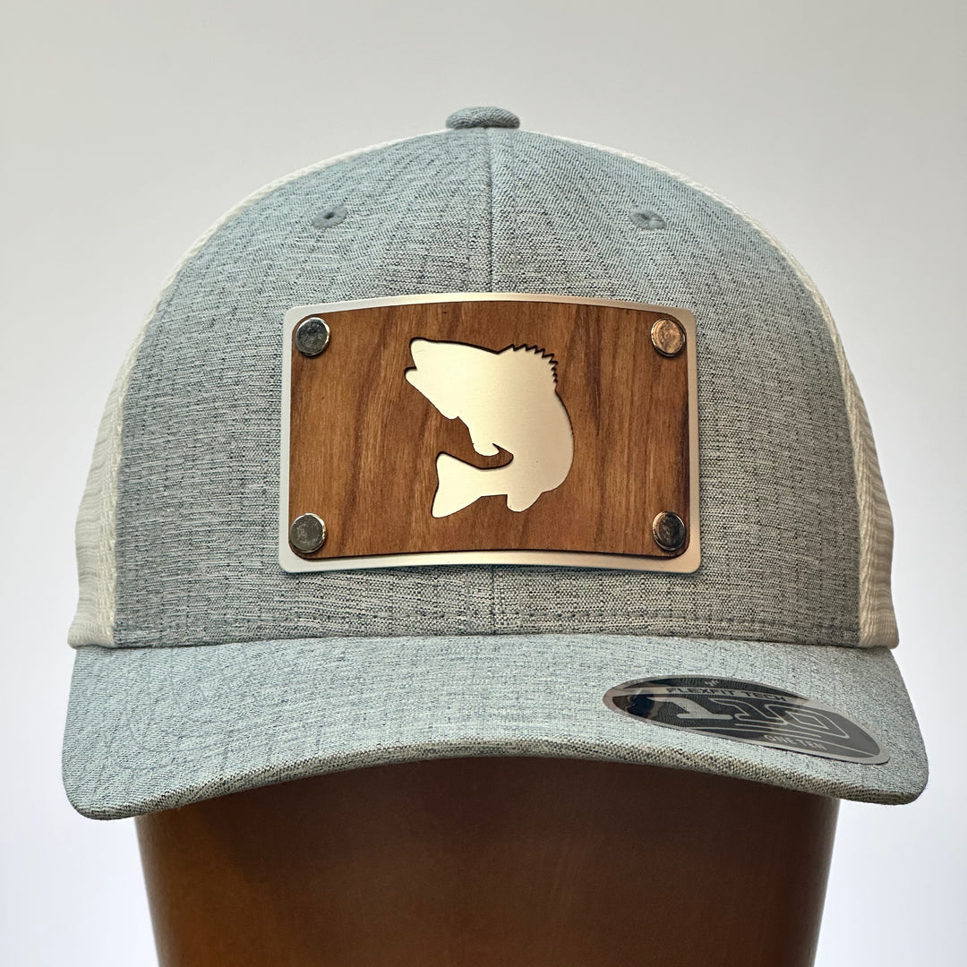 A cherry wood and metal patch with a walleye silhouette featured on a bright silver patch. Riveted to a heather grey and white flexfit trucker hat.