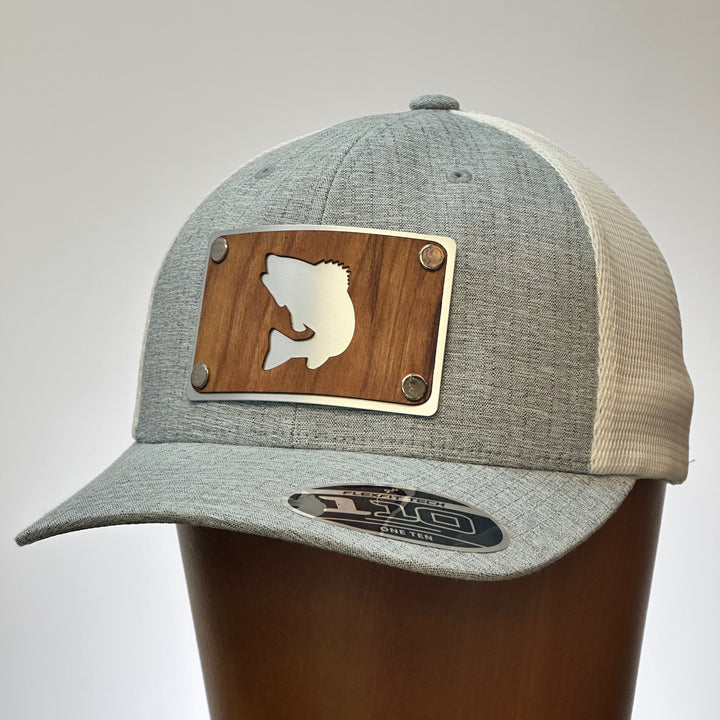 A cherry wood and metal patch with a walleye silhouette featured on a bright silver patch. Riveted to a heather grey and white flexfit trucker hat.