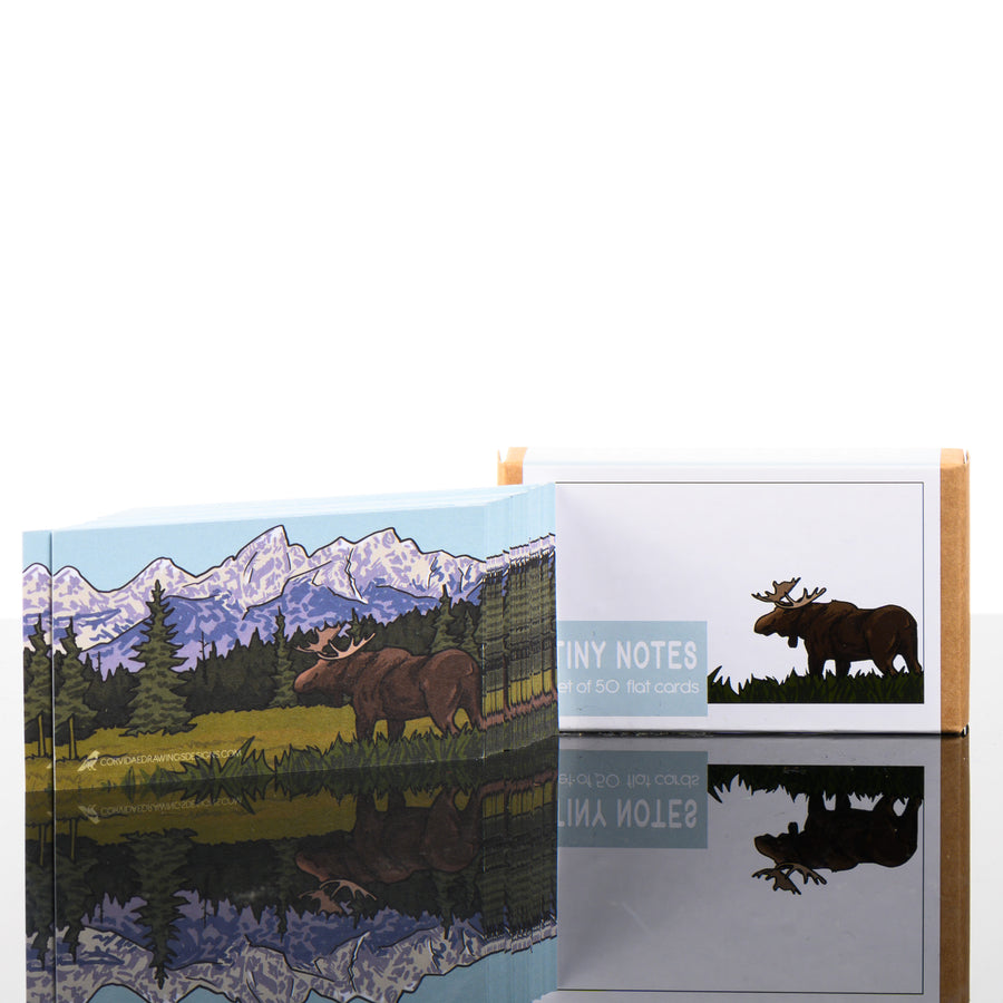 This 50 note card pack features a cute drawing of a moose in a pine tree forest with snowy mountains in the background.