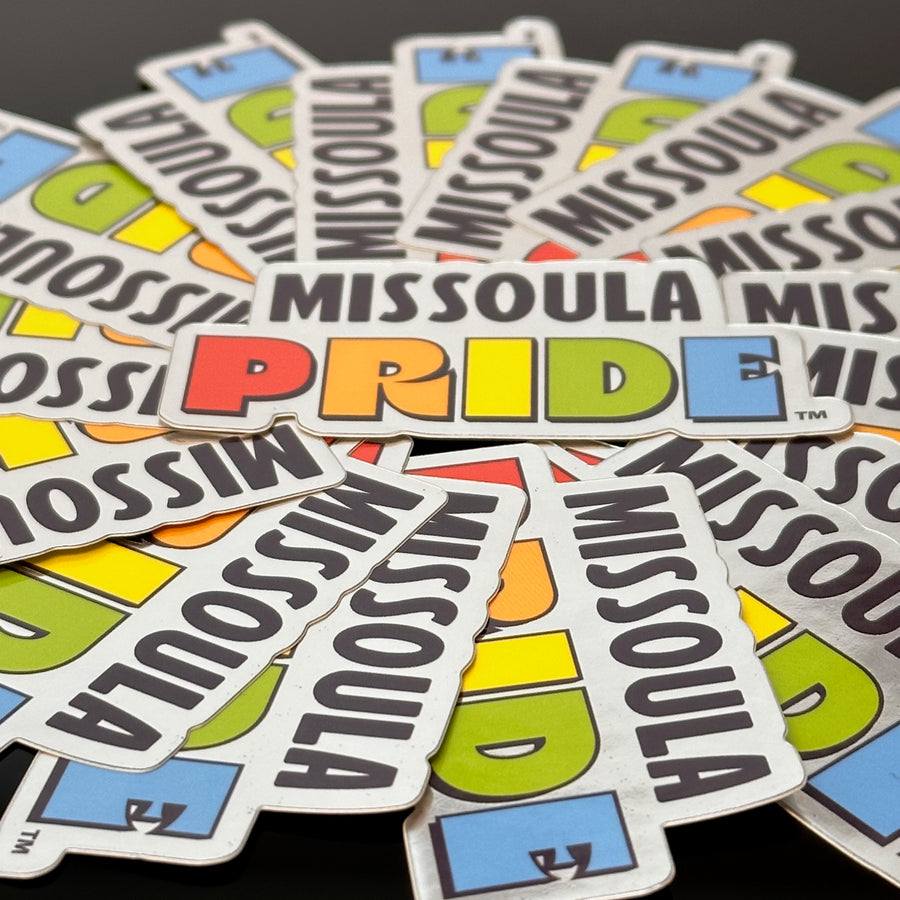 Circled group of Missoula PRIDE stickers with "PRIDE" in rainbow tones, on a chrome background, closeup