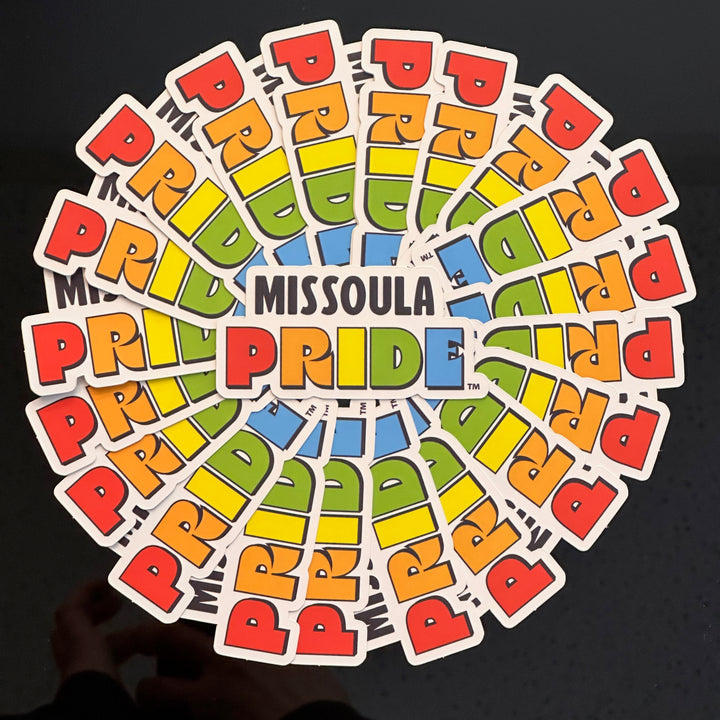 Circled group of Missoula PRIDE stickers with "PRIDE" in rainbow tones on a white background