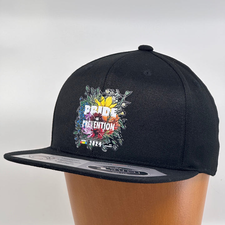 Black flat bill hat featuring the 2024 Missoula PRIDE design Pride is Prevention, 3/4 view (left)