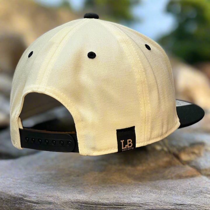 Back of an ivory and black flat bill hat, on a rock