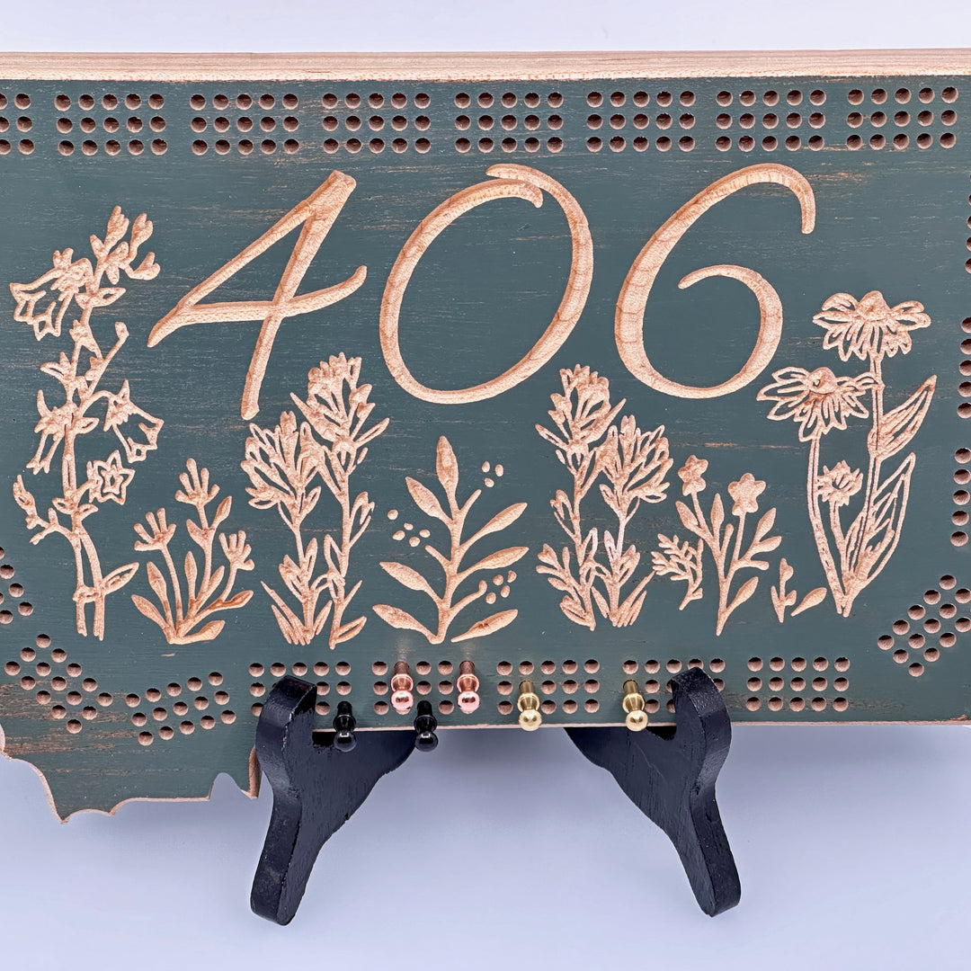 Knotty Pine Woodworks 406 Wildflower  Cribbage Board (sage color with natural wood accents, detail)--this made in Montana wood cribbage board is in the shape of Montana, and features the Montana state area code (406) and wildflowers engraved in the front.