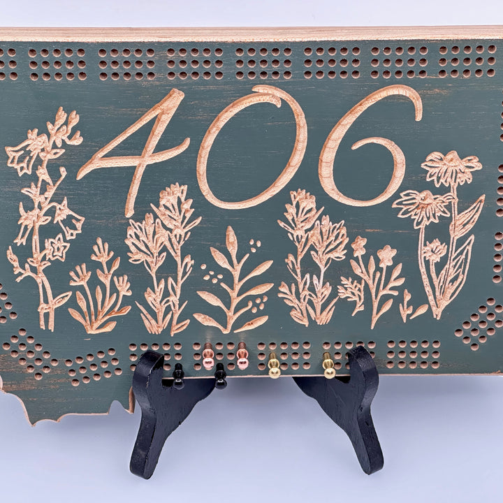 Knotty Pine Woodworks 406 Wildflower  Cribbage Board (sage color with natural wood accents, detail)--this made in Montana wood cribbage board is in the shape of Montana, and features the Montana state area code (406) and wildflowers engraved in the front.