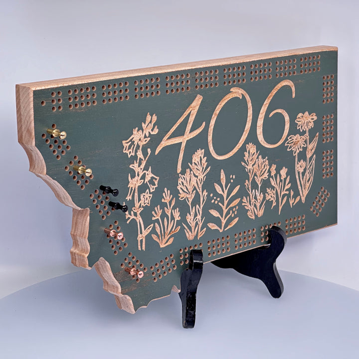 Knotty Pine Woodworks 406 Wildflower  Cribbage Board (sage color with natural wood accents, front)--this made in Montana wood cribbage board is in the shape of Montana, and features the Montana state area code (406) and wildflowers engraved in the front.