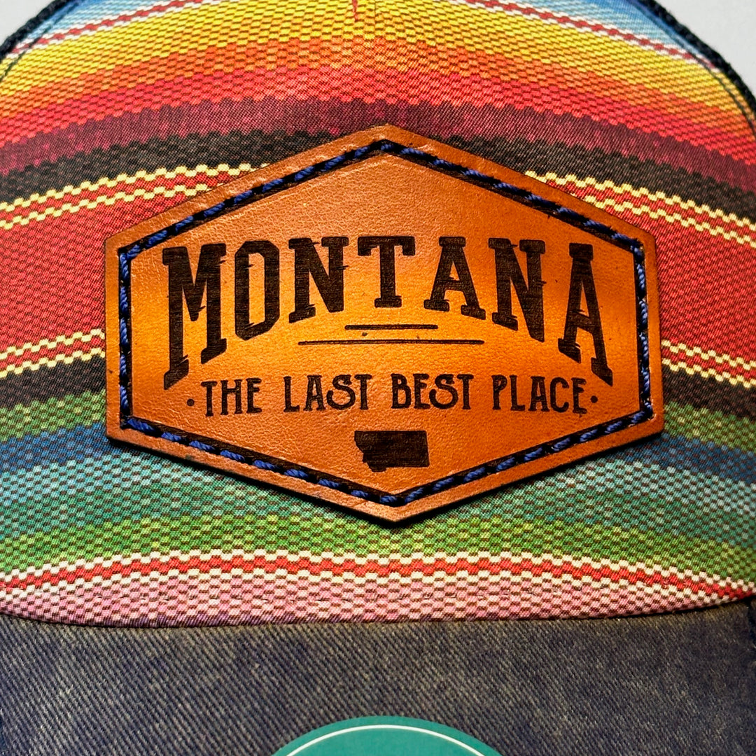 A close up of A poncho printed trucker hat with a thick leather patch that says Montana, The Last Best Place.