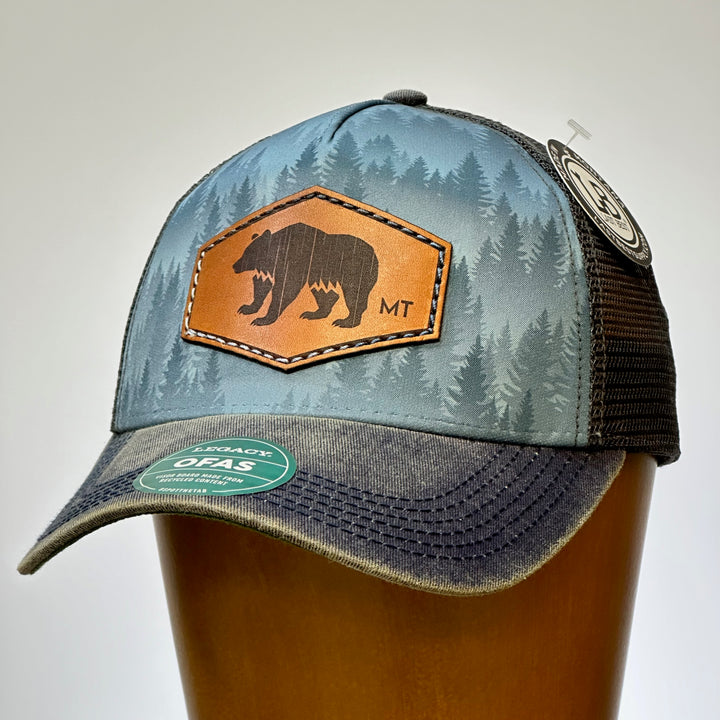 This is the front face of a hand dyed leather patch, made in Montana, in the shape of a Bear with the letters MT underneath, legacy trucker hat