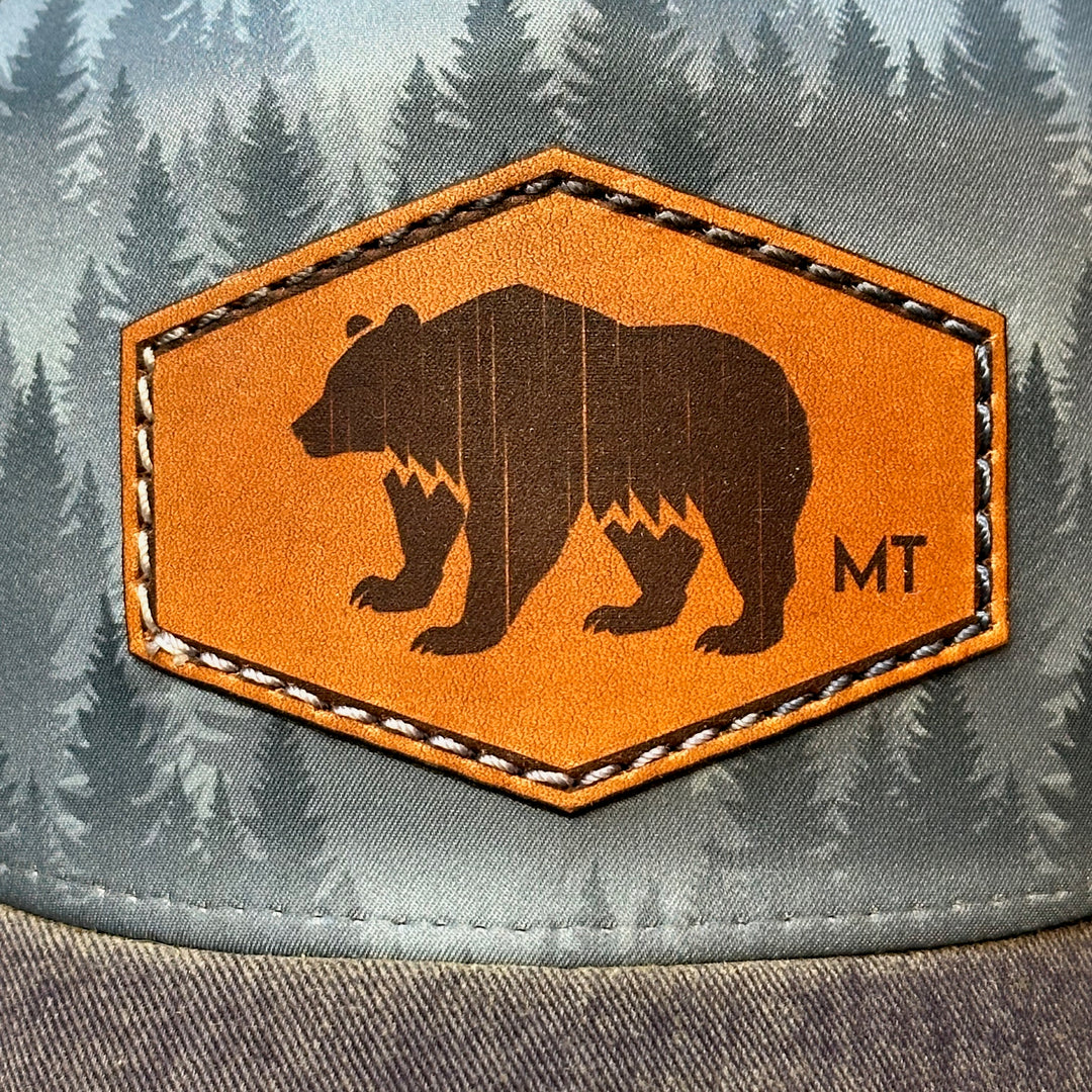 This is a zoomed in image of a hand dyed leather patch, made in Montana, in the shape of a Bear with the letters MT underneath, legacy trucker hat