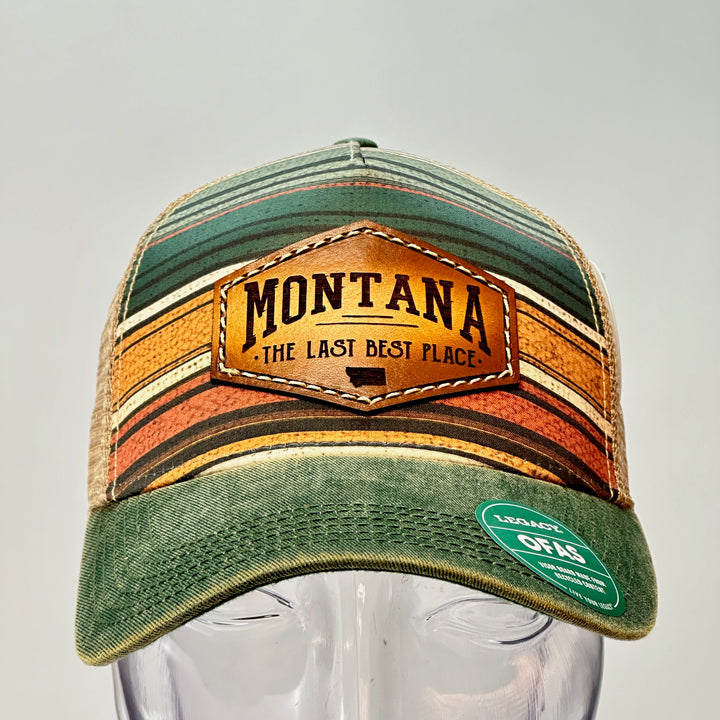 A  green lined printed Legacy trucker hat with a thick leather patch that says Montana, The Last Best Place.