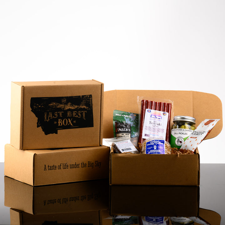 A Montana made snack gift box called The Last Best Box featuring teriyaki beef sticks, classic dill pickles, caramel cookie waffles, huckelberry fudge, buffalo soldier cashews and churro kracklin kamut.