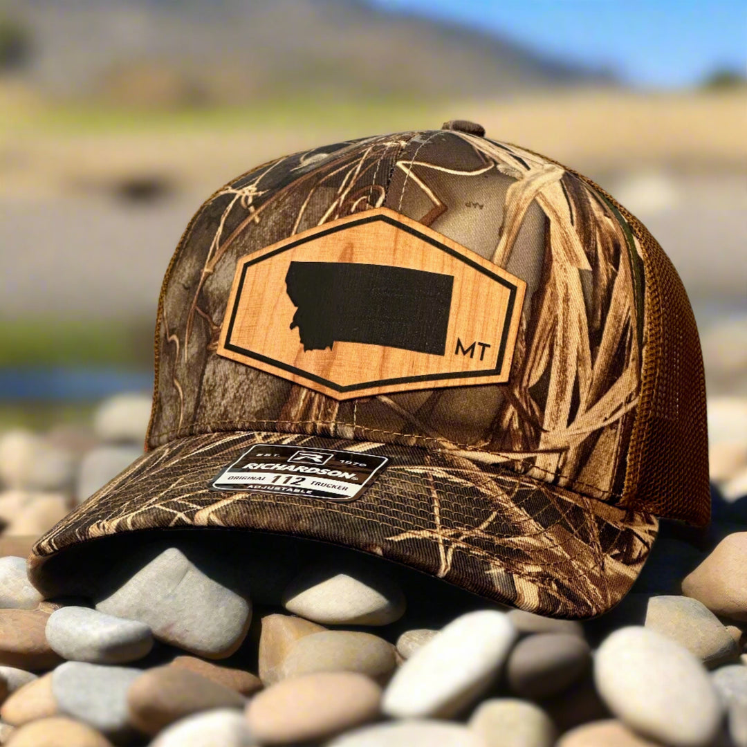 A wood patch hat with the shape of Montana in a hexagon and mossy oak camo hat