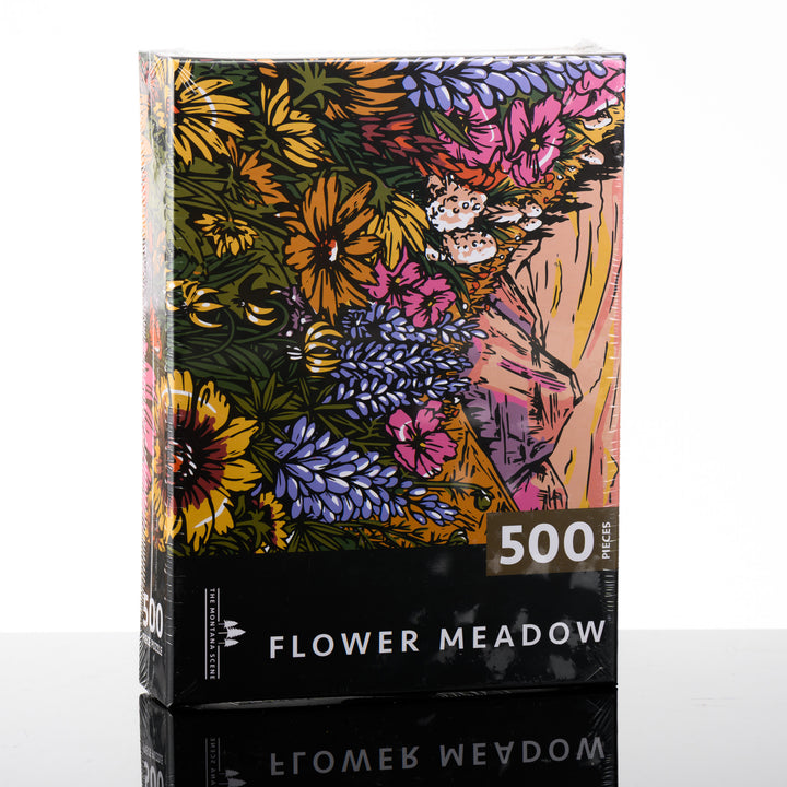 A puzzle box featuring a 500 piece puzzle by The Montana Sene featuring a flower meadow with a mountain.