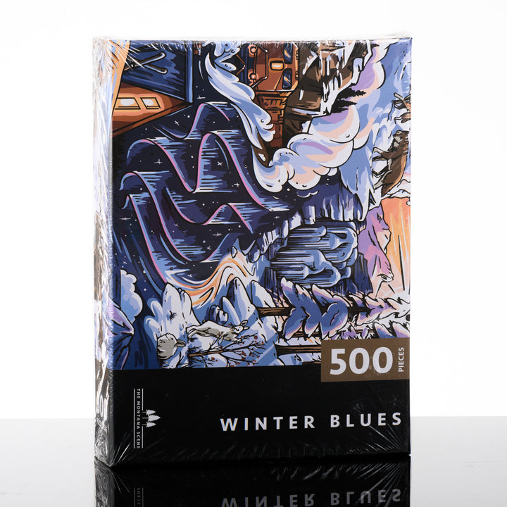 This hand drawn 500 piece puzzle is titled Winter Blues and features a snowy landscape with a cozy cabin and is made by The Montana Scene in Kalispell, Montana; image depicts box front.