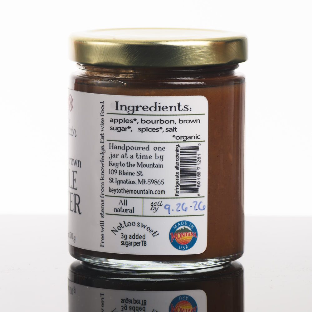 A picture of the front of a 6 ounce jar of Montana grown apple butter listing the ingredients, organic apples, bourbon, organic brown sugar, organic, spices, salt