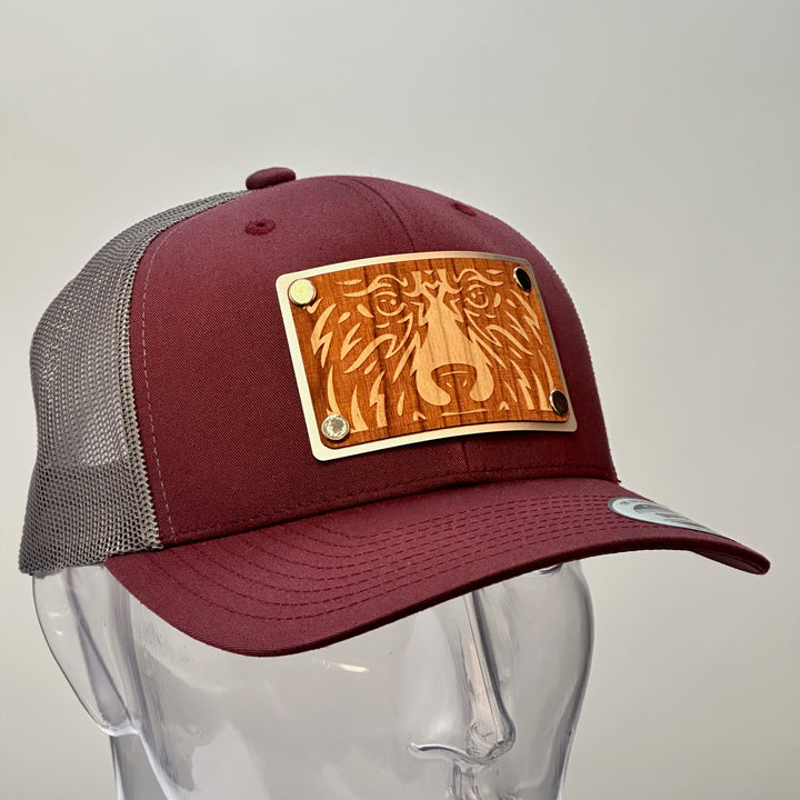 A side view of a made in Montana bear face cherry wood patch maroon and grey trucker hat.