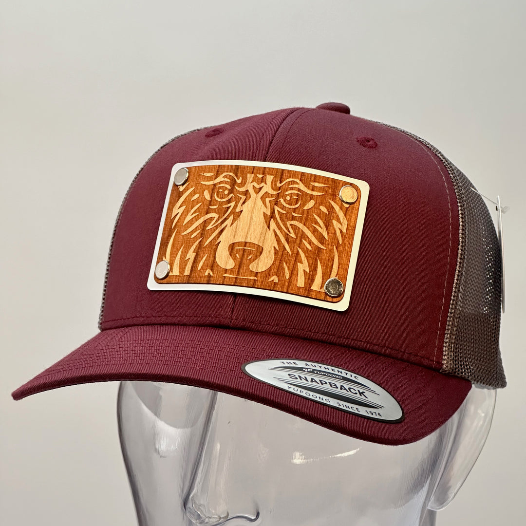 A side view of a made in Montana bear face cherry wood patch maroon and grey trucker hat.