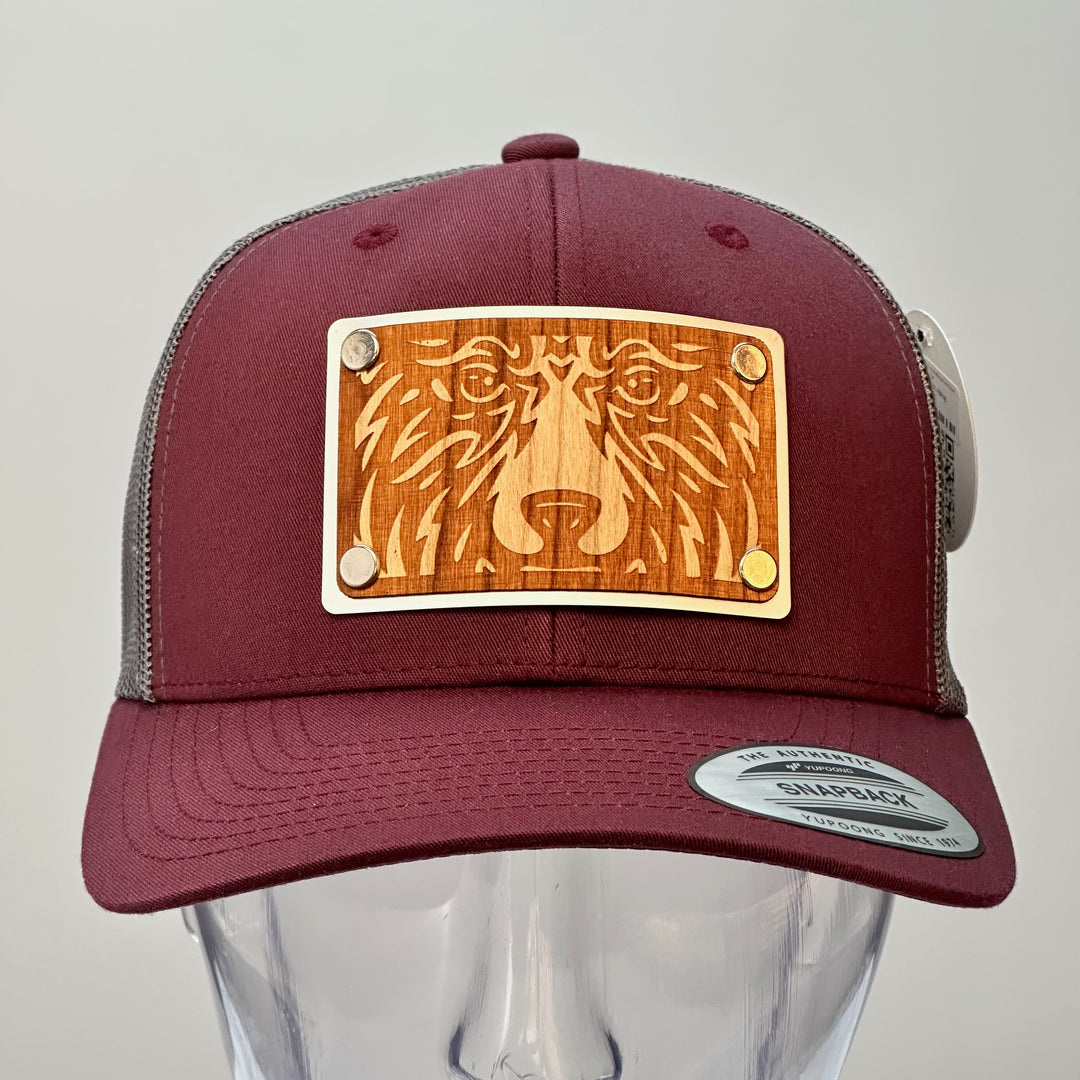 A front view of a made in Montana bear face cherry wood patch maroon and grey trucker hat.