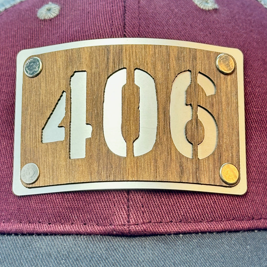 A close up of a made in Montana 406 Walnut and metal patch riveted to a maroon and grey trucker hat.