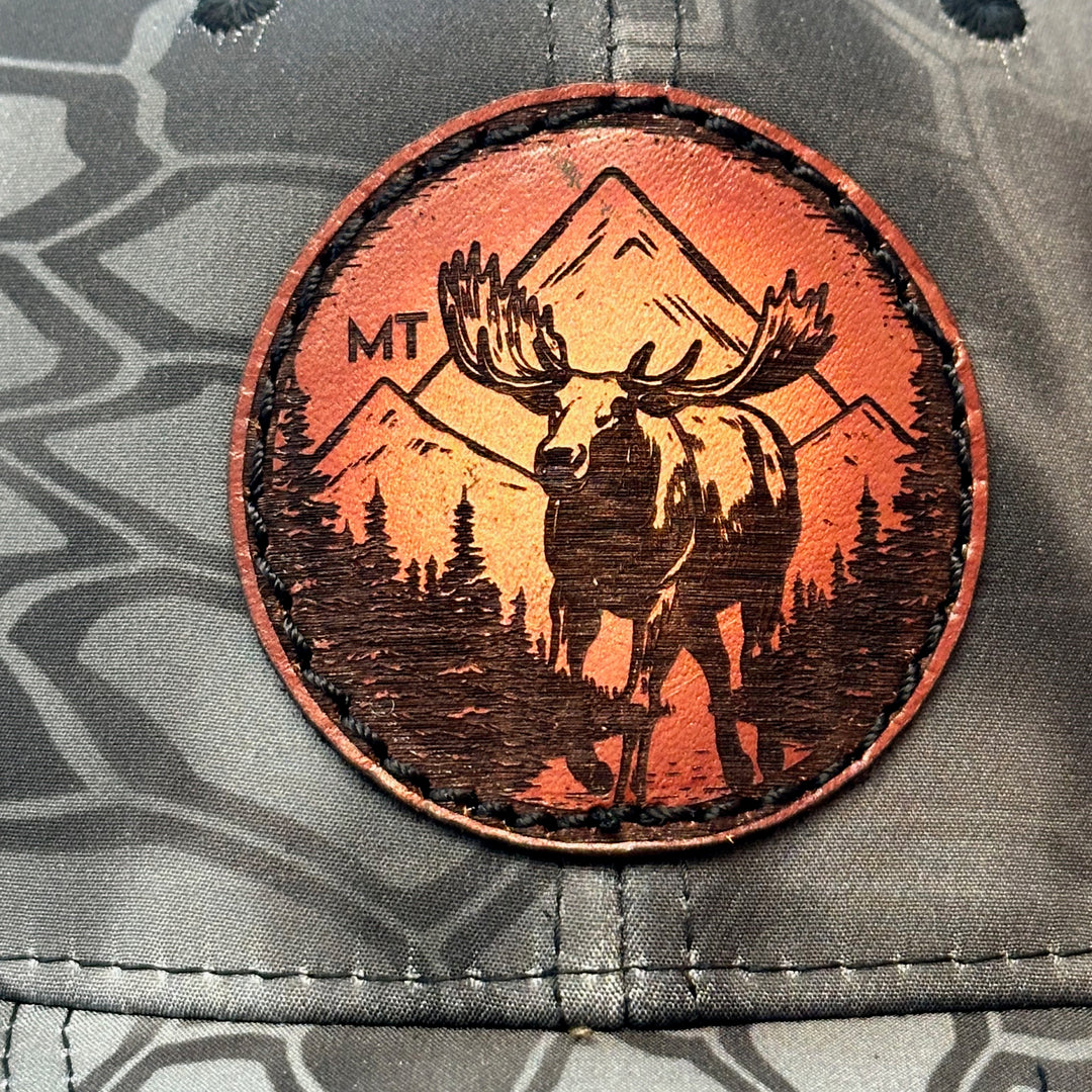 A close up made in Montana leather patch hat featuring a moose, sewn on a grey Kryptek trucker Hat.