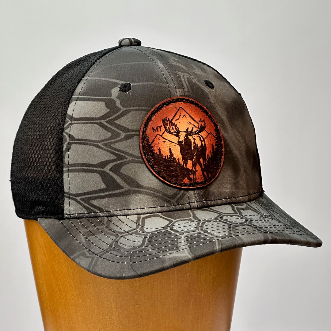 A made in Montana leather patch hat featuring a moose, sewn on a grey Kryptek trucker Hat.