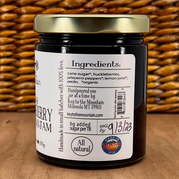 A 6oz jar of Key to the Mountain's Montana made Wild Huckleberry Jalepeno Jam Ingredient's list: organic cane sugar, huckleberries, organic jalapeño peppers, organic lemon juice pectin.