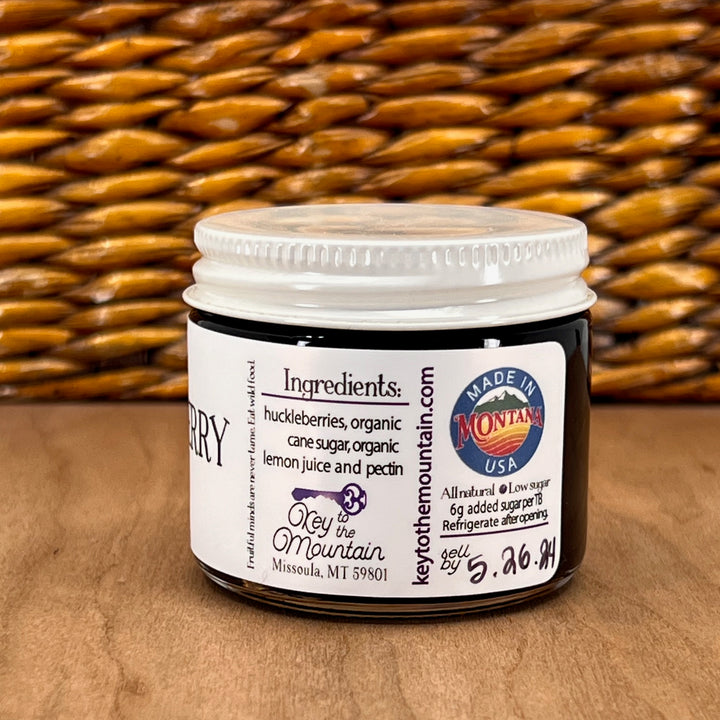 A 2oz jar of Key to the Mountain's, Montana handmade Wild Huckleberry Jam ingredients list: huckleberries, organic cane sugar, organic lemon juice, and pectin.